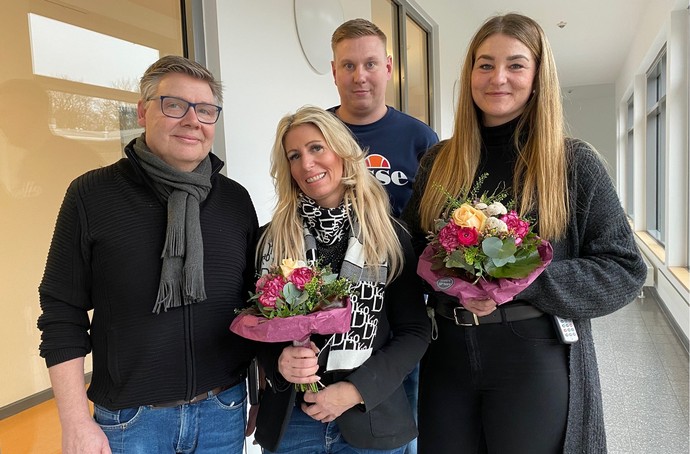 Zwei Männer und zwei Frauen stehen in einem Flur und lächeln in die Kamera